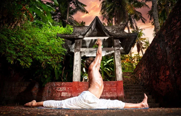 緑あふれる屋外でハヌマーン・アーサナをとる1人の男性