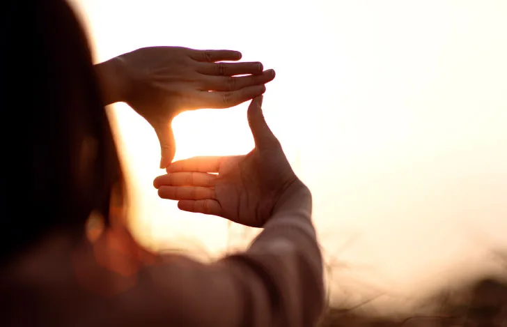 夕陽に向かって手で四角いフレームを作る女性
