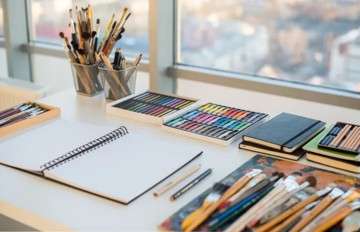 窓辺の机に置かれたスケッチブックや色鉛筆や絵筆