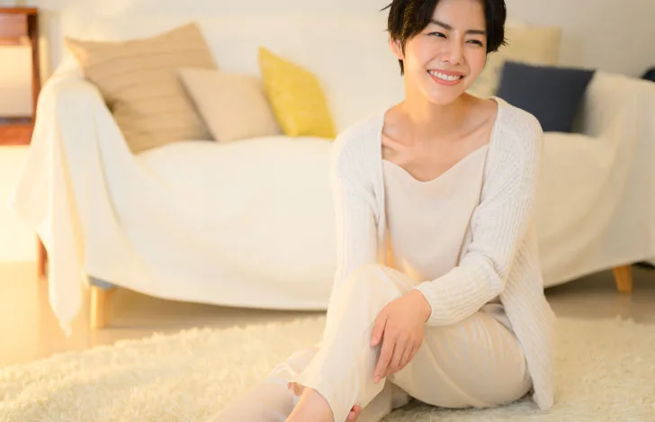 室内で女性が自分の足を触りながら笑顔でくつろぐ様子